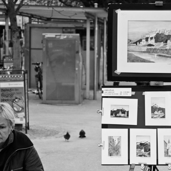 black and white photo of an elderly lady selling her paintings on the street