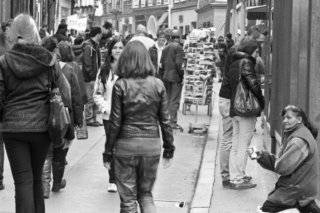 black and white photo of a crowded tourist street with a beggar